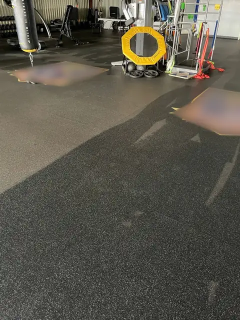 A gym floor half cleaned of storm dust: dark clean rubber in the foreground, pale dust beyond, and gym equipment behind
